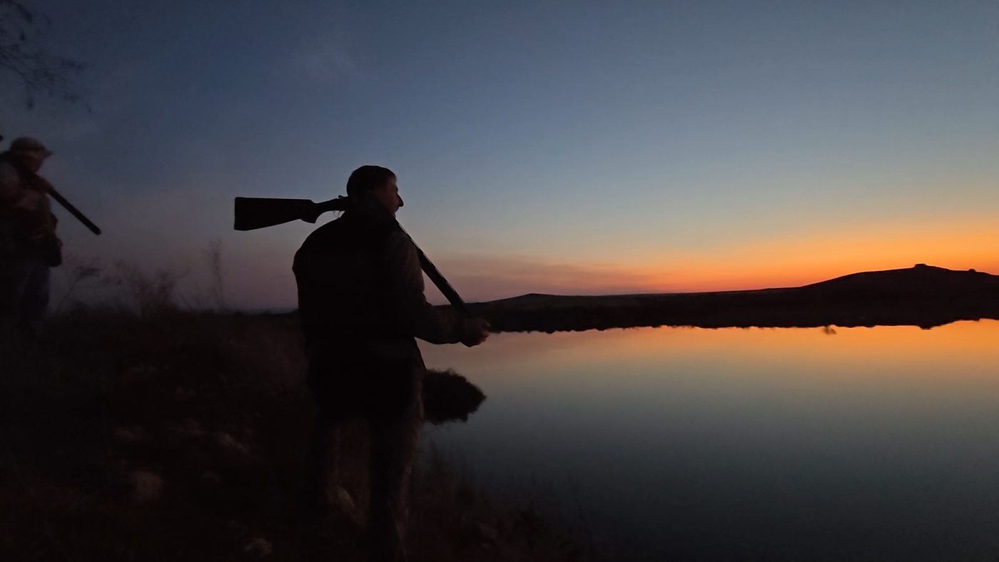Hunter carrying his rifle home at dusk over still water
